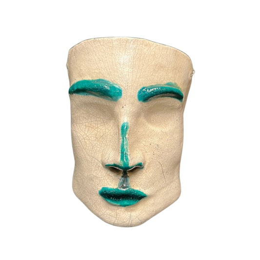 Front view of a ceramic face sculpture with teal accents on a white background