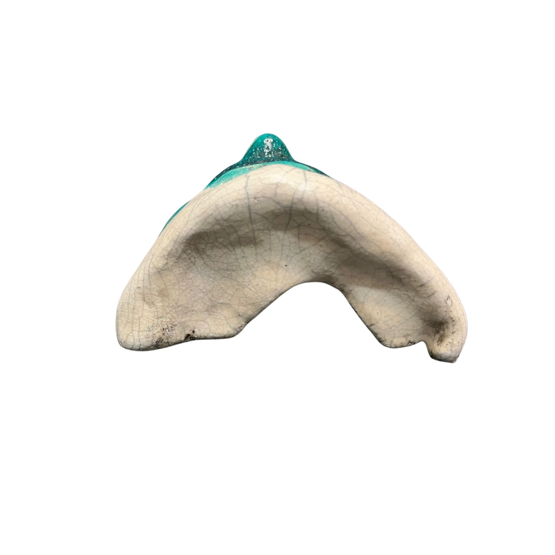 Bottom view of a ceramic face sculpture with teal accents on a white background